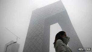 A woman walks past the new China Central Television (CCTV) building amid heavy fog in Beijing, 5 Dec 2011