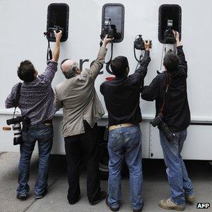 Press photographers take pictures of a prison van leaving the City of Westminster Magistrates Court in London