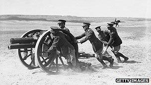 Soldiers pushing a gun over sand