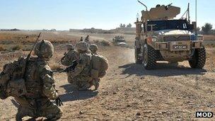 Soldiers crouching by a roadside in Afghanistan with an armoured vehicle