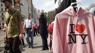 Tourists pass a vendor's stand selling hooded tops - one saying 'I (heart) NY' - in Fifth Avenue, New York City