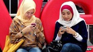 Two women use social media on their mobiles in Jakarta on 11 February 2012