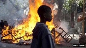 A boy stands in front of a burning barricade set up by anti-government protestors during clashes with police in Senegal"s capital Dakar, February 19, 2012.