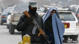 An Afghan policeman keeps watch as a woman pass by a check point in Kabul