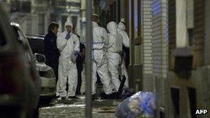 Police and members of a forensics team stand at the entrance to a mosque following petrol bomb attack in Anderlecht
