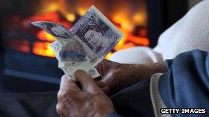 A old person holding money in front of a gas fire