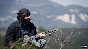A Syrian opposition fighter crouches in hills near Idlib, 24 March