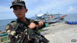 A Philippine soldier stands guard next to fishing boats at a pier in Masinloc town, Zambales province, 230km from Scarborough Shoal, 18 May 2012