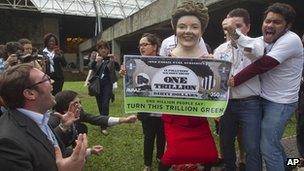 Environmental activists, one portraying Brazilian President Dilma Rousseff holding a banner symbolizing "dirty money" made from fossil fuel subsidies