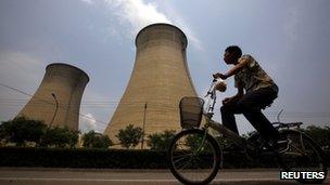 A man rides his bicycle past the cooling tower and chimneys from a coal-burning power station in Beijing