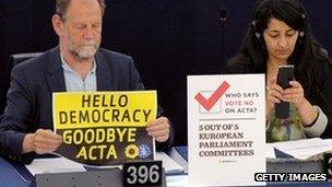 Member of European Parliament holds sign reading "Hello democracy, goodbye Acta"