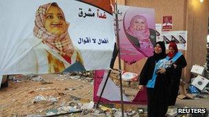 Majdah al-Fallah (L) and Hannan Bachir, candidates for the Justice and Construction Party walk past defaced campaign posters in Tripoli