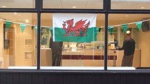 Fflag Cymru a fflagiau gwyrdd yr Eisteddfod mewn ffenestr siop