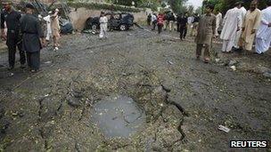 Security officials and residents gather near a crater caused by a bomb attack in Peshawar on Monday