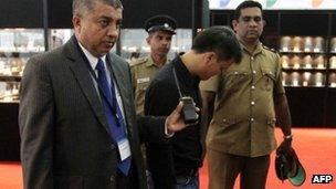 A Sri Lankan security official (L) and uniformed police escort a Chinese national (C) who was accused of stealing a $13,800 diamond by swallowing it