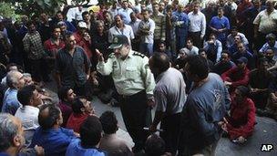 A police officer debates with workers protesting about delayed wages in front of the ministry of industry in Tehran on 14 August