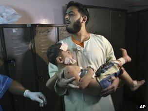 A Palestinian man carries a boy injured in an Israeli air strike in Gaza (7 October 2012)