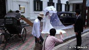 A photographer positions a bride for a picture for her wedding photo album in front of a colonial style hotel, rickshaw and old cars in downtown Hanoi on August 26, 2010.