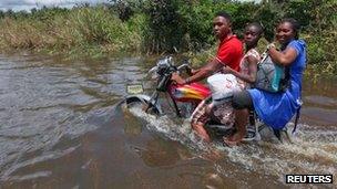 Мужчина едет на мотоцикле с пассажирами по затопленной дороге в общине Патани в штате Дельта Нигерии, 15 октября 2012 г.