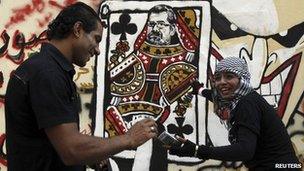 Youths admire a mural on Cairo's Mohammed Mahmoud street showing Mohammed Mursi's head on a queen of clubs playing card