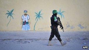 A Nigerian policeman working with the African Union Mission in Somalia walks by a painted image on a newly built wall during a foot patrol near Lido beach in Somalia's capital, Mogadishu
