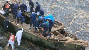 Police officers investigating a wooden boat with Korean language markings on Sado island, Niigata City, on 28 November 2012