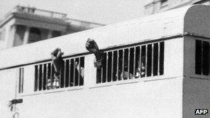 Eight of the Rivonia trial defendants leaving the Palace of Justice in Pretoria on 16 June 1964 with their fists raised in defiance through the barred windows of the prison car