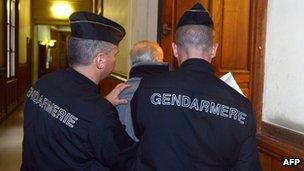 French police guard a defendant at an earlier appearance in the trial in Paris, 3 December