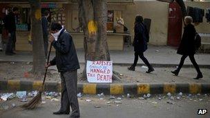 An Indian municipal worker sweeps a road as a placard, demanding death penalty for rapists, is placed on a sidewalk in New Delhi, India.