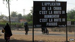 Malians pass a billboard left by Islamist militants in the northern city of Gao, reading: "Enforcing Sharia is the road to happiness, it is the road to paradise"