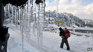 An Indian laborer walks carrying a cooking gas cylinder on a snow covered road in Shimla, India, Saturday, Jan. 19, 2013.