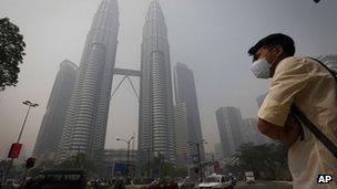 A pedestrian wearing a mask waits to cross a main road in front of Petronas Twin Tower covered by haze in Kuala Lumpur, Malaysia, 24 June 24 2013