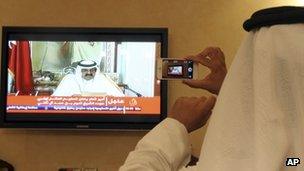 A man prepares to take a picture with his mobile photo of a televised address by Qatar's Emir Sheik Hamad bin Khalifa Al Thani