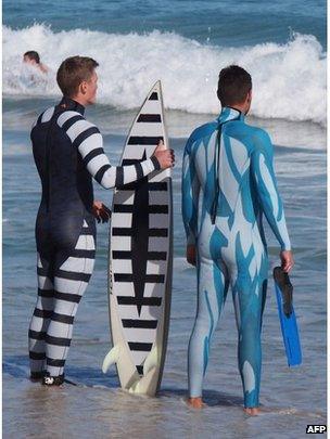 A surfer wearing a black and white striped wetsuit and black and white striped surfboard next to a diver wearing a blue wetsuit