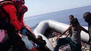 A picture released by the Italian coast guards shows coast guards puling a man as they help immigrants out of their dinghy on August 8, 2013 in the Mediterranean, off Lampedusa
