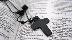 A crucifix necklace lying on an open Bible