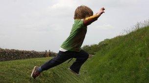 A young boy jumping over a grassy ditch