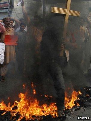 A Christian man in Lahore holding a cross jumps over burning tyres during a protest against a twin suicide bomb attack on a church in Peshawar, 22 September 2013