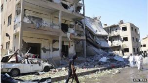A man holds a weapon as he walks past damaged buildings at a site hit by what activists say was a car bomb in Raqqa province, eastern Syria August 29, 2013