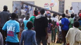 People use a pole to batter a shop doorway during clashes with police in Lusaka April 19, 2016