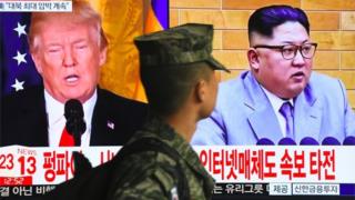 A South Korean soldier walks past a TV screen showing pictures of US President Donald Trump and North Korean leader Kim Jong Un at a railway station in Seoul