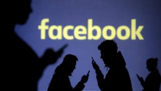   An image showing silhouettes of mobile phone users next to the Facebook logo projection. 