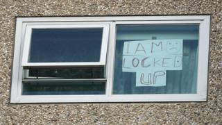 Sign in the window of a locked-down unit reads: "I am locked up"
