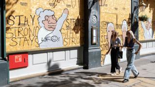 Two young women walk past a morale-boosting message written on plyboard of the boarded-up Garrick Arms pub on Charing Cross Road in London - 20 August 2020