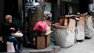 A woman sits under a poster for presidential candidates along a street in Buenos Aires