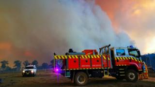 A fire truck and another vehicle parked in front of a massive cloud of smoke from the Long Gully Road fire in October