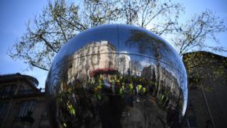 Demonstrators are reflected in a sculpture during yellow vest protest in Paris
