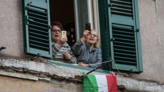 women-in-italy-use-phones-out-of-their-window-smiling