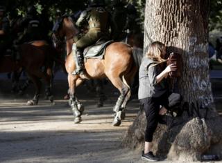 A woman takes cover behind a tree during clashes