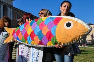 Women holding several drawings of sardines and a giant sardine-shaped stuffed cushion take part in the "Sardine Movement" rally in Rome, 14 December